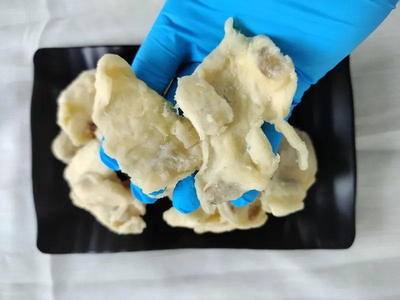 Soft-dried soursop pieces on a black plate, one gloved hand holding it