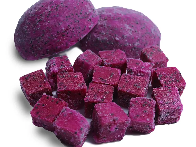 Two whole red dragon fruits behind a pile of freeze-dried dragon fruit cubes, cut out on white.