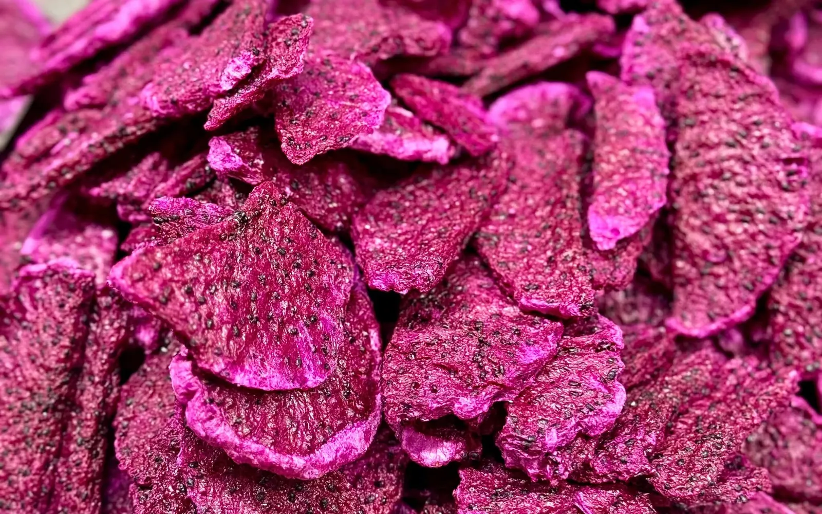 Full-frame close-up of bright pink freeze-dried dragon fruit slices.