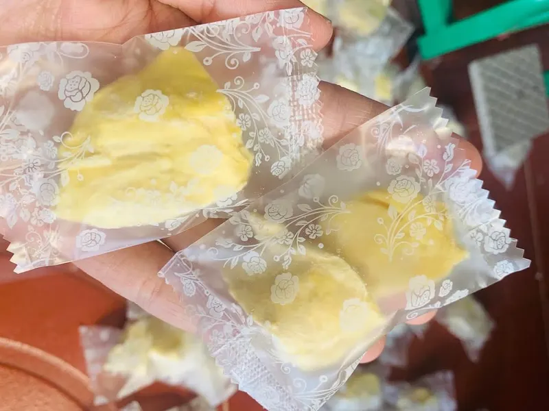 Hand holding small patterned clear sachets each containing a piece of freeze-dried durian.
