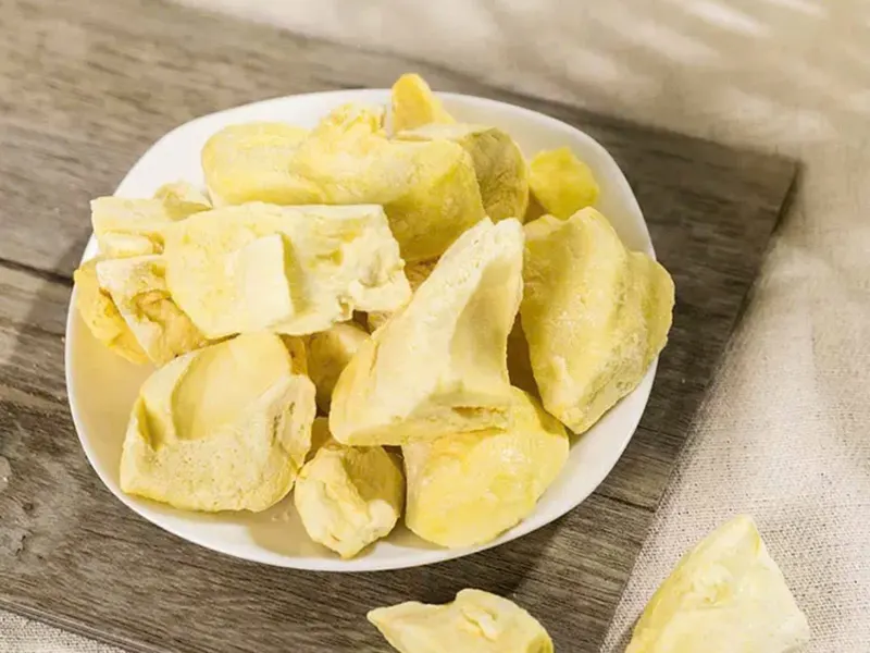 White plate of freeze-dried durian chunks on a wooden board.