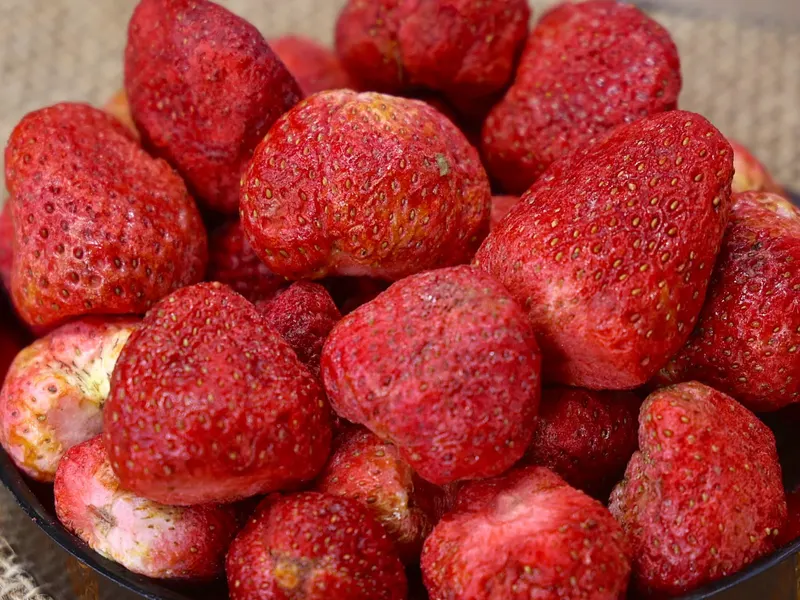 Dark wooden bowl of whole freeze-dried strawberries on a woven mat.