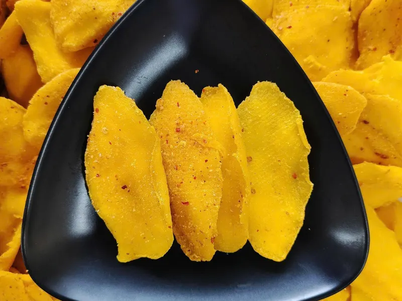 Rounded triangular black plate holding four chilli-dusted dried mango slices.
