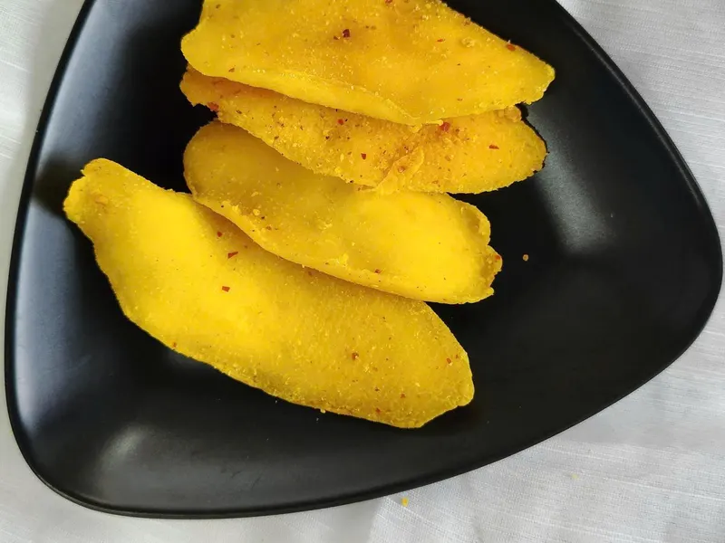 Four chilli-dusted mango slices on a black triangular plate.