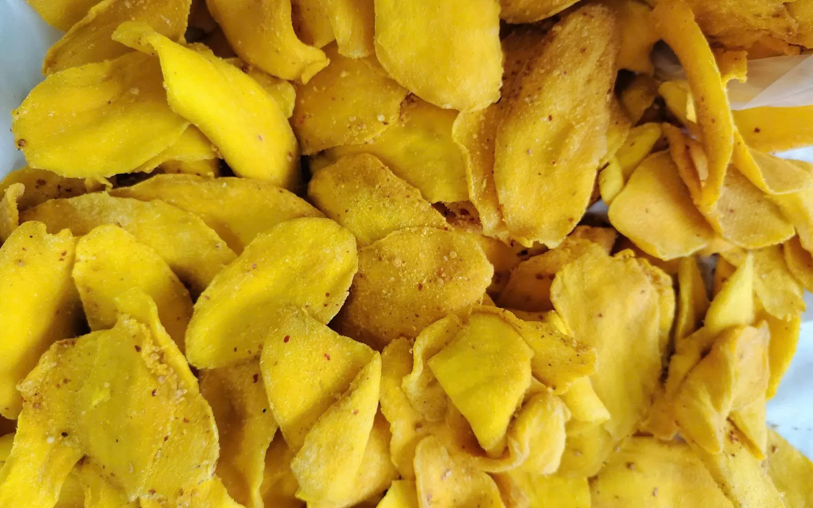 Full-frame close-up of chilli-dusted soft-dried mango slices piled on a tray.