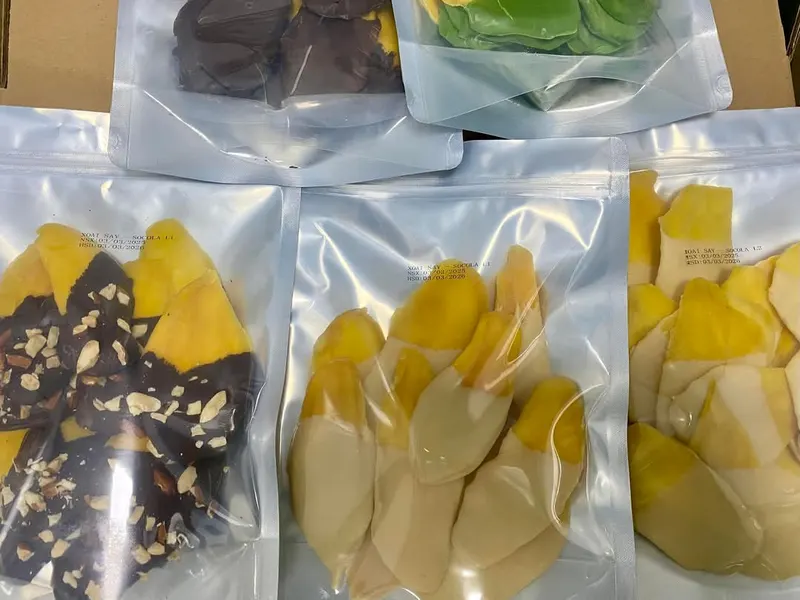 Vacuum-sealed packs of chocolate-dipped mango laid out on a carton.