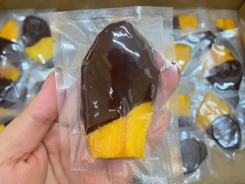 Hand holding a vacuum pack containing a chocolate-dipped mango slice.
