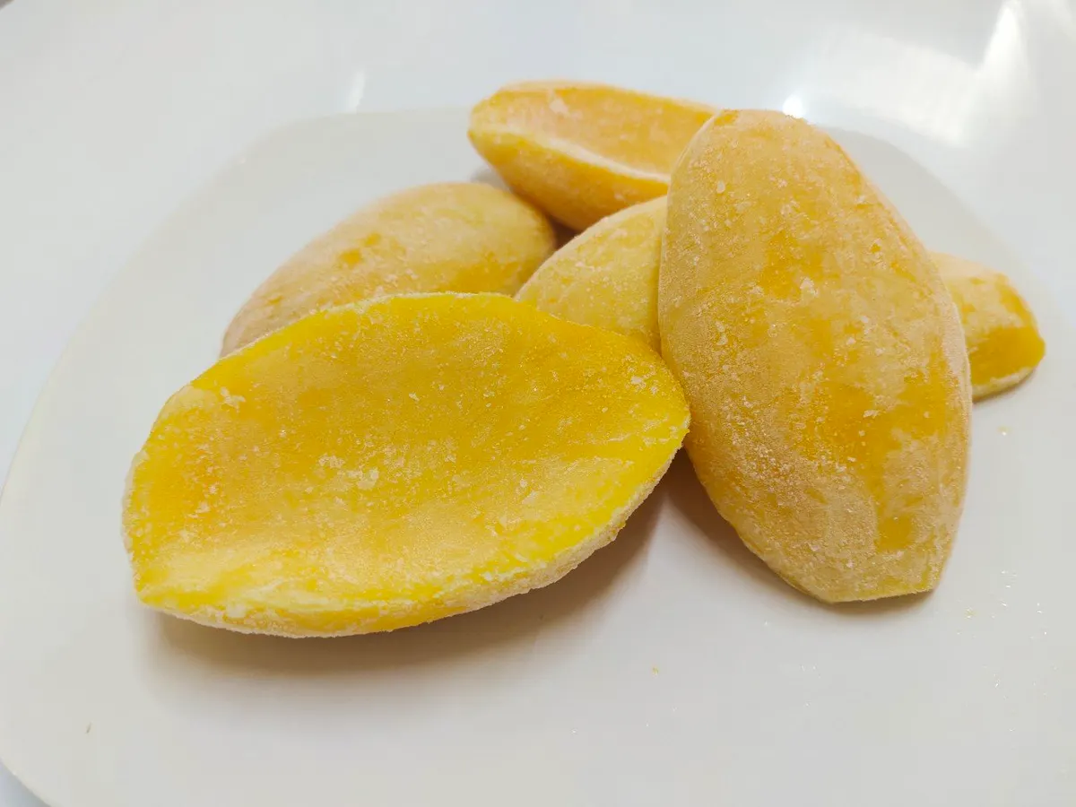 Three frozen mango cheeks on a plain white plate, one cut to show the flesh.