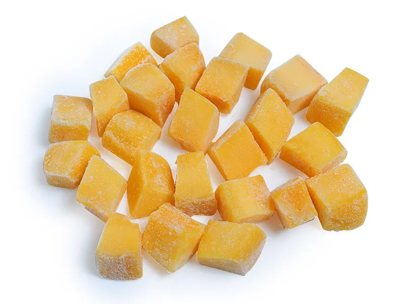 About twenty frozen mango dice scattered on a white background.