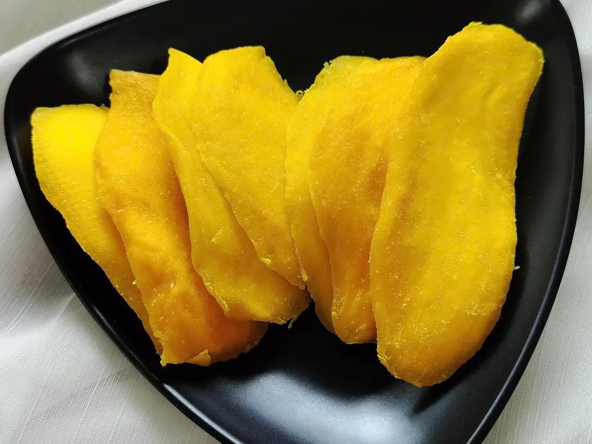 Three large soft-dried mango slices on a black triangular plate.