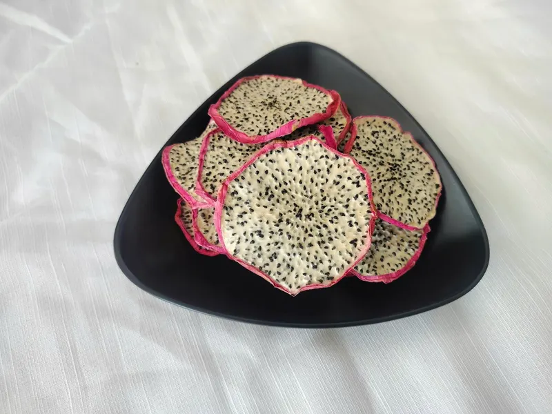 Top-down view of soft-dried white dragon fruit slices on a black triangular plate
