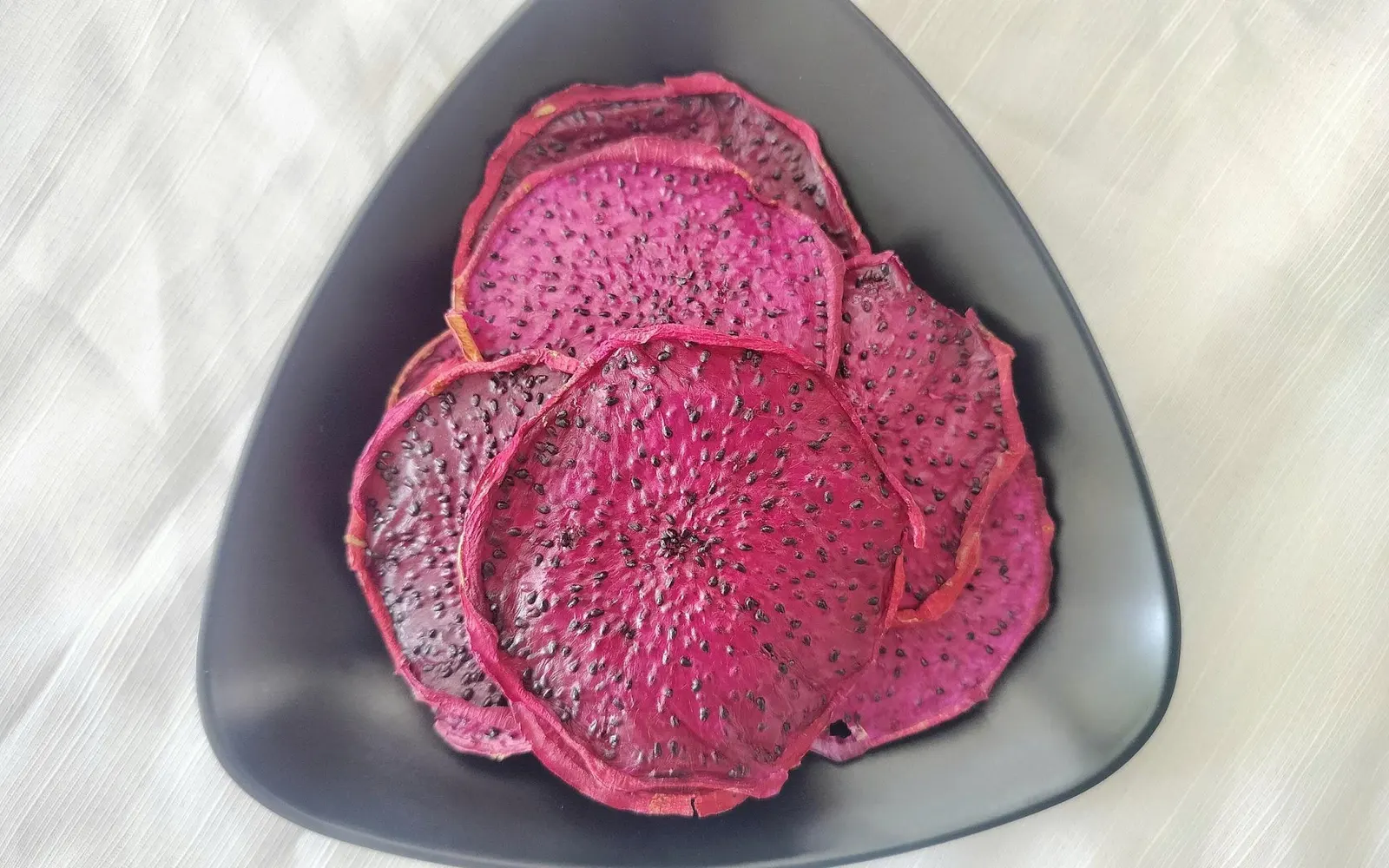 A few overlapping slices of soft-dried red dragon fruit on a black plate.