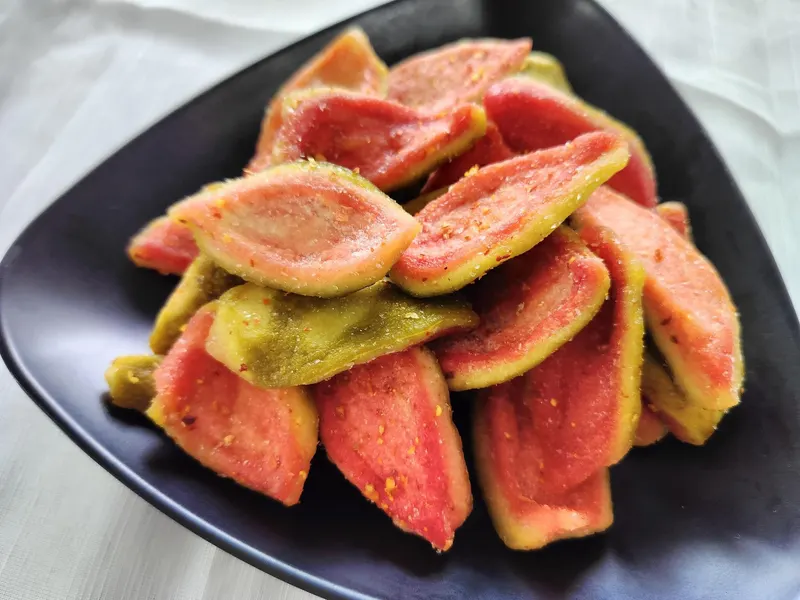 Top-down close-up of soft-dried pink guava slices on a black plate.