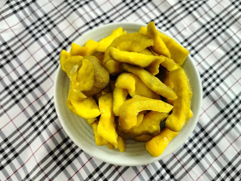White bowl of yellow soft-dried guava pieces on a black-and-white checked cloth.