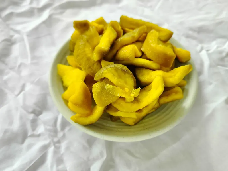 Pale bowl of yellow soft-dried guava pieces on white cloth.