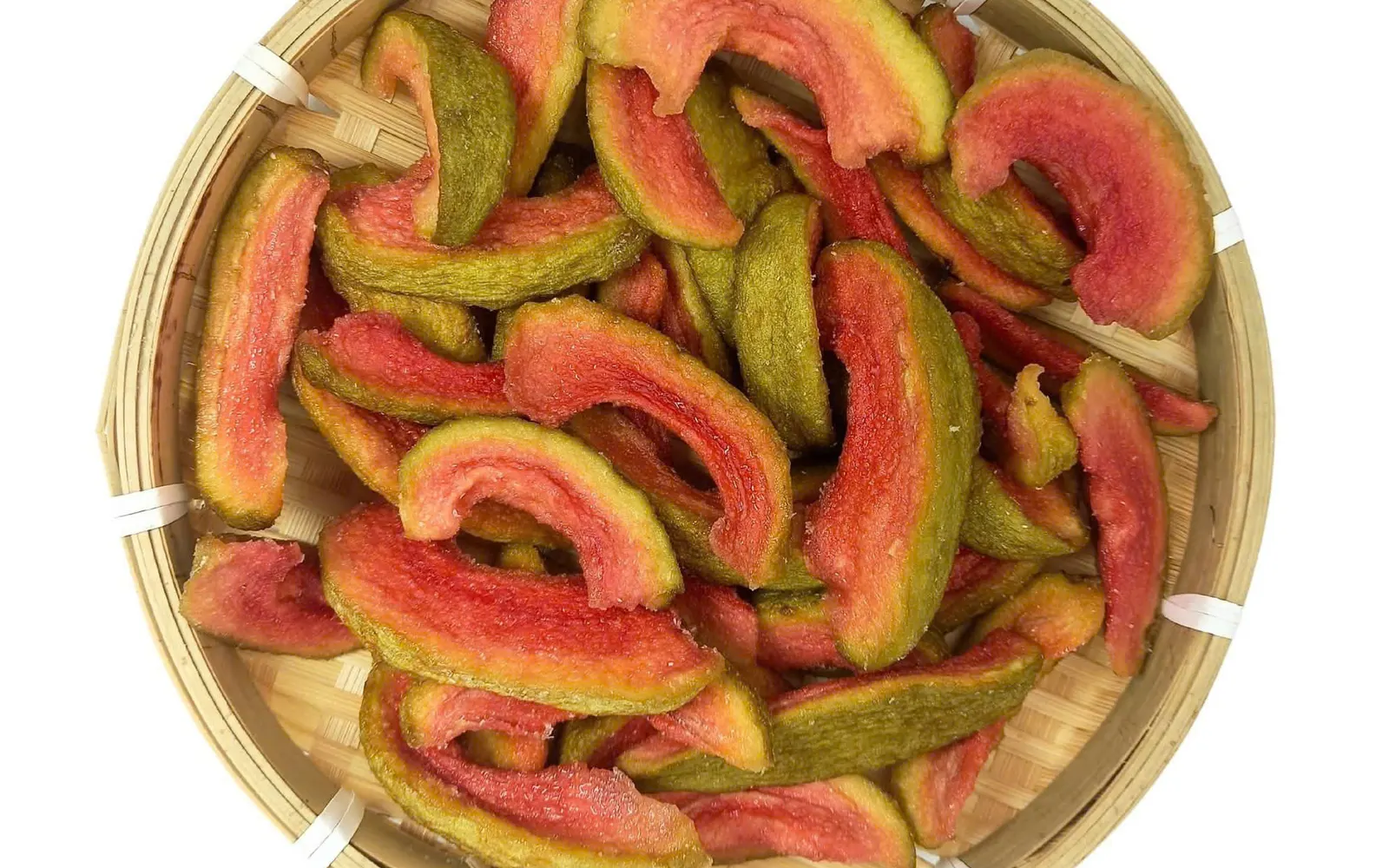 Round bamboo winnowing tray filled with soft-dried pink guava slices, shot from above.