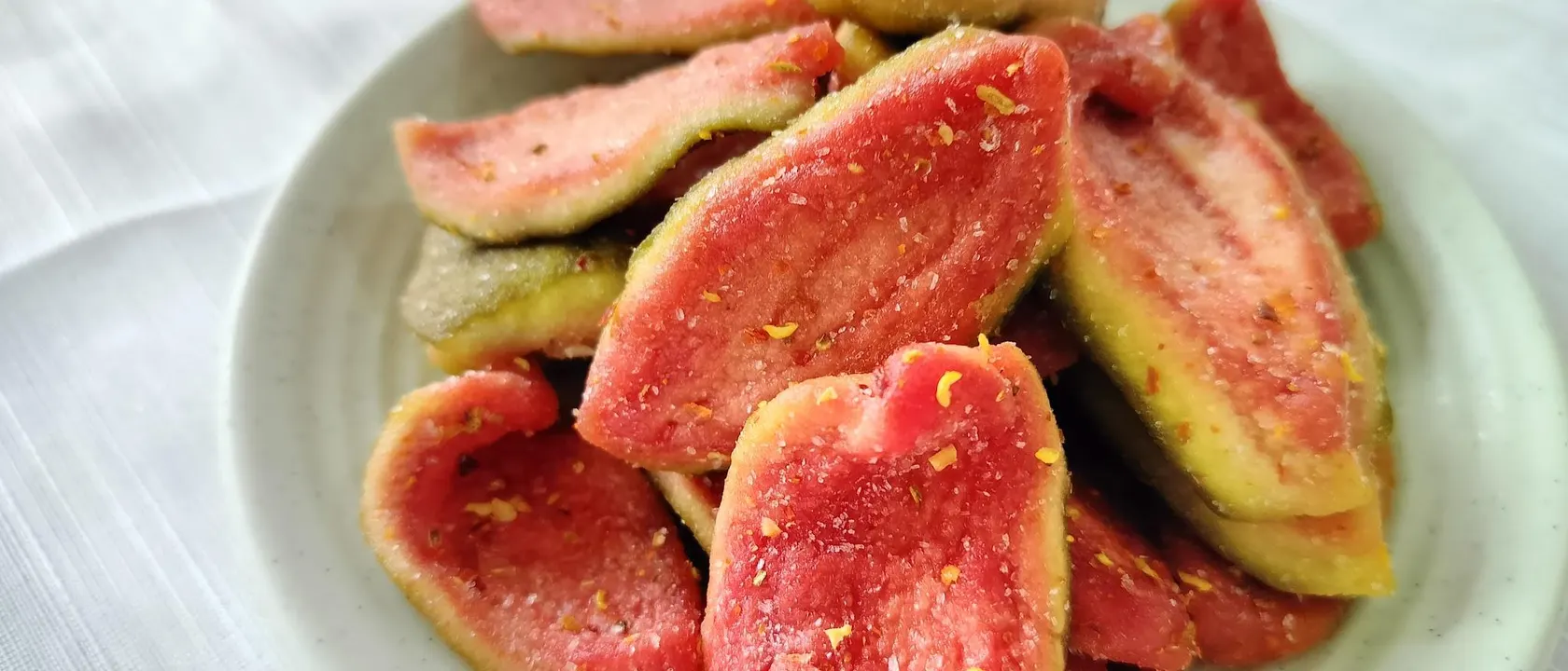 Close-up of soft-dried pink guava slices with green rind edges on a pale plate.