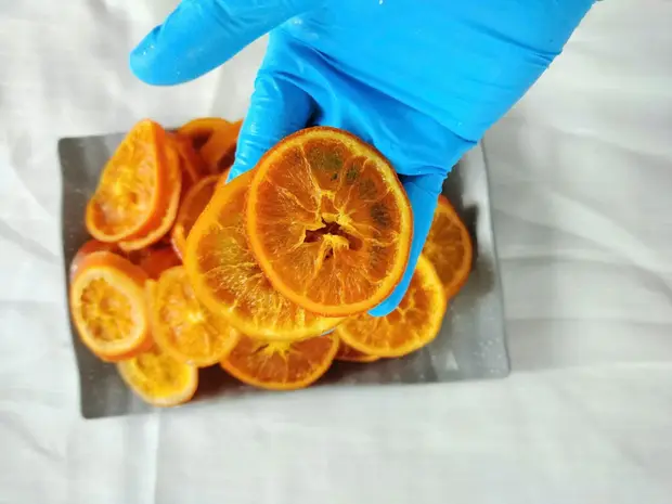 Gloved hand picking a soft-dried orange slice from a grey tray.