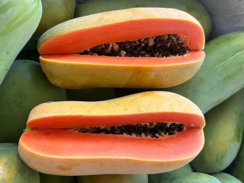 Halved papayas showing orange flesh and black seeds resting on a pile of whole green papayas.