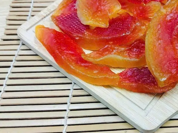Glossy red-orange soft-dried papaya slices on a white wooden board over a bamboo mat.