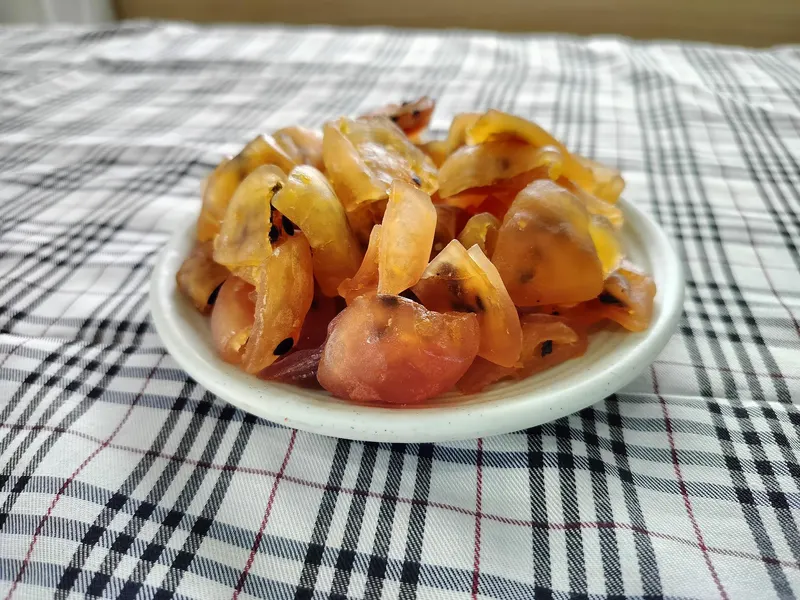 White plate of amber soft-dried passion fruit pieces with black seeds on a checked cloth