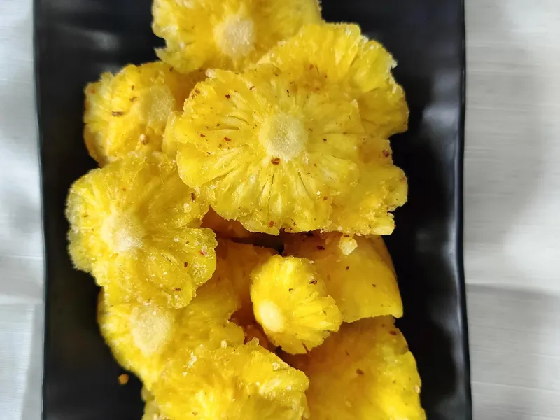 Straight top-down view of soft-dried pineapple rings on a black rectangular plate