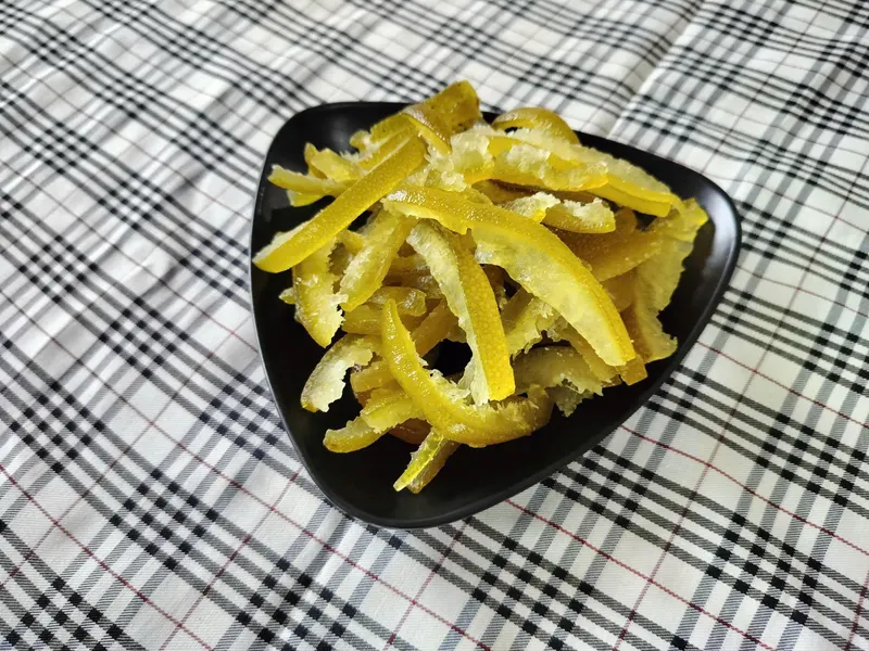 Black triangular plate of dried pomelo peel strips on a checked cloth.