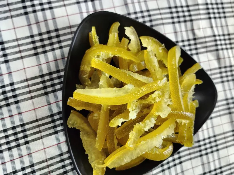 Vertical shot of a black plate of dried pomelo peel strips on a checked cloth.