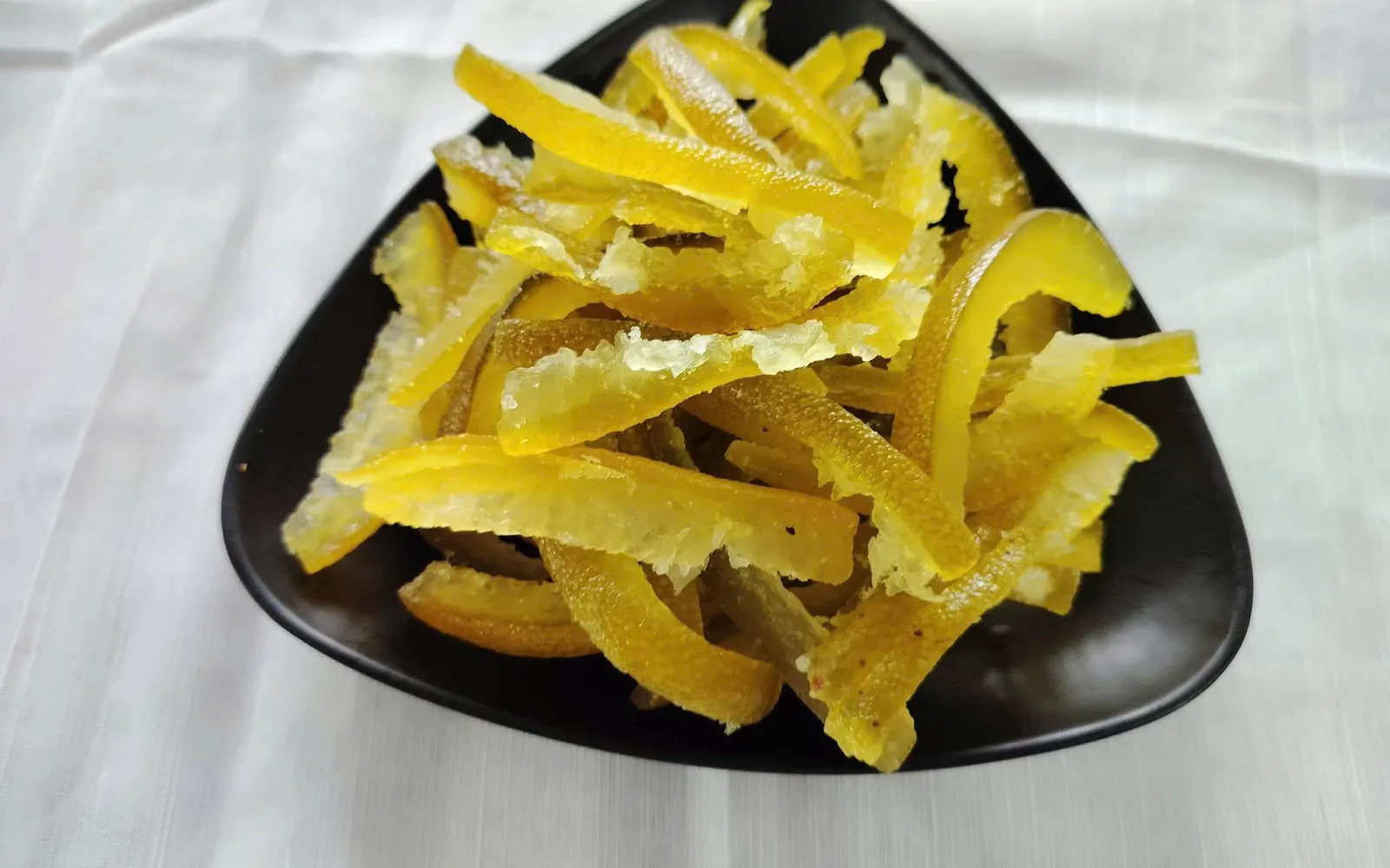 Black triangular plate heaped with sugar-coated dried pomelo peel strips.