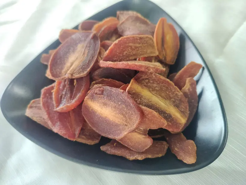 Close-up of a dark plate heaped with soft-dried sapodilla slices.