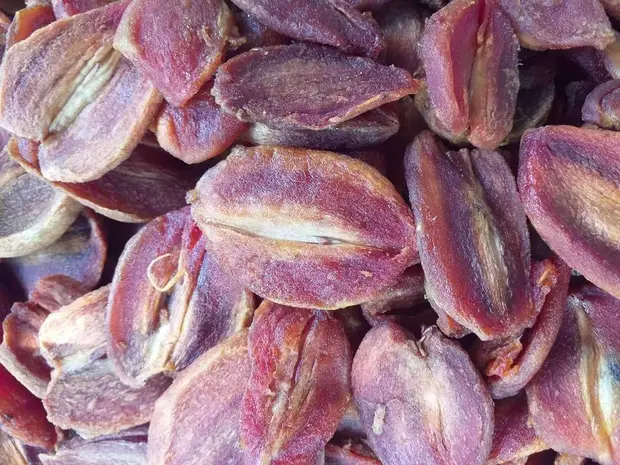 Close-up of bulk purple-brown soft-dried sapodilla slices filling the frame.