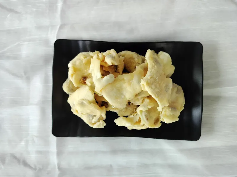 Black rectangular plate of cream soft-dried soursop pieces on white cloth.