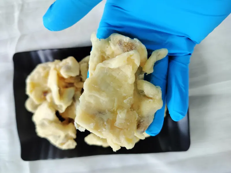 Gloved hand lifting a large soft-dried soursop piece above a black plate.