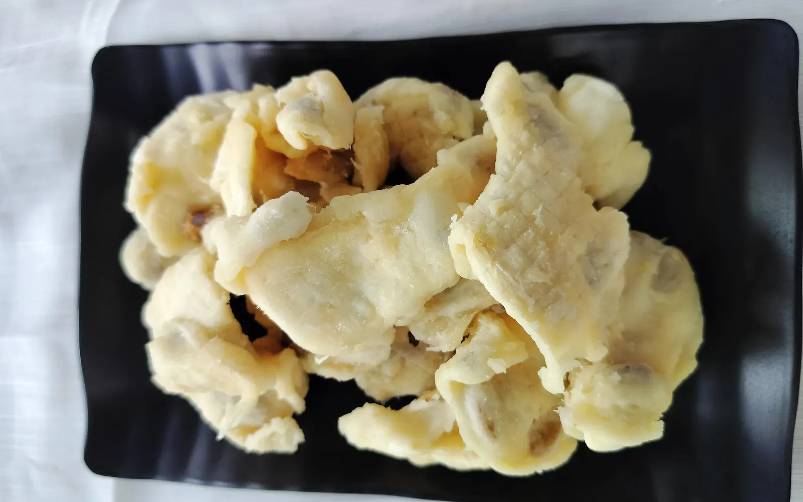 Top-down view of a black plate heaped with soft-dried soursop pieces.