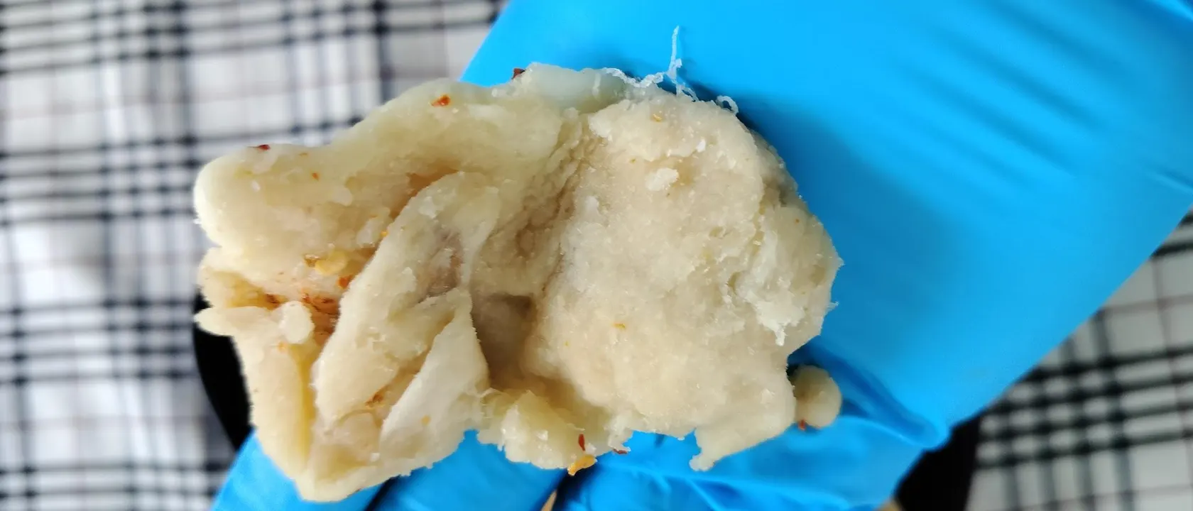 Gloved hands lifting chilli-salted soft-dried soursop pieces above a black plate.