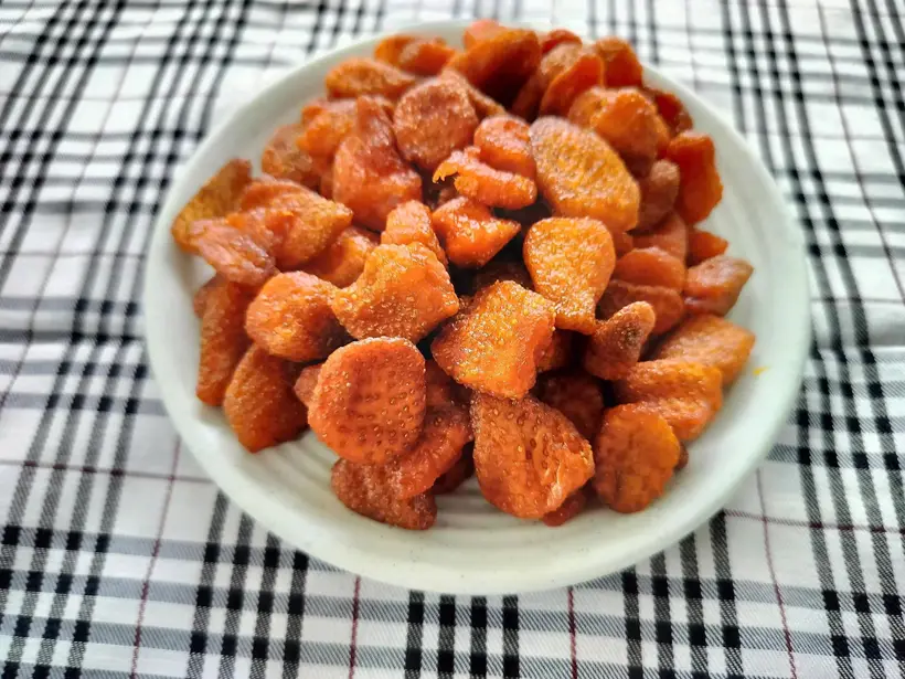 White plate heaped with orange-red soft-dried strawberries on a checked cloth.